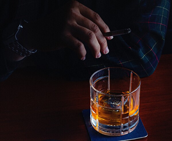 Aschenbecher, Zigarre in der Hand und starker Alkohol im Glas