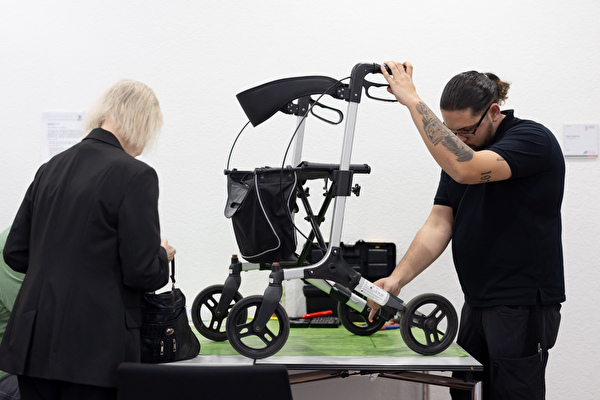 Ein Mann kontrolliert den Rollator einer älteren Frau auf Funktionstüchtigkeit.