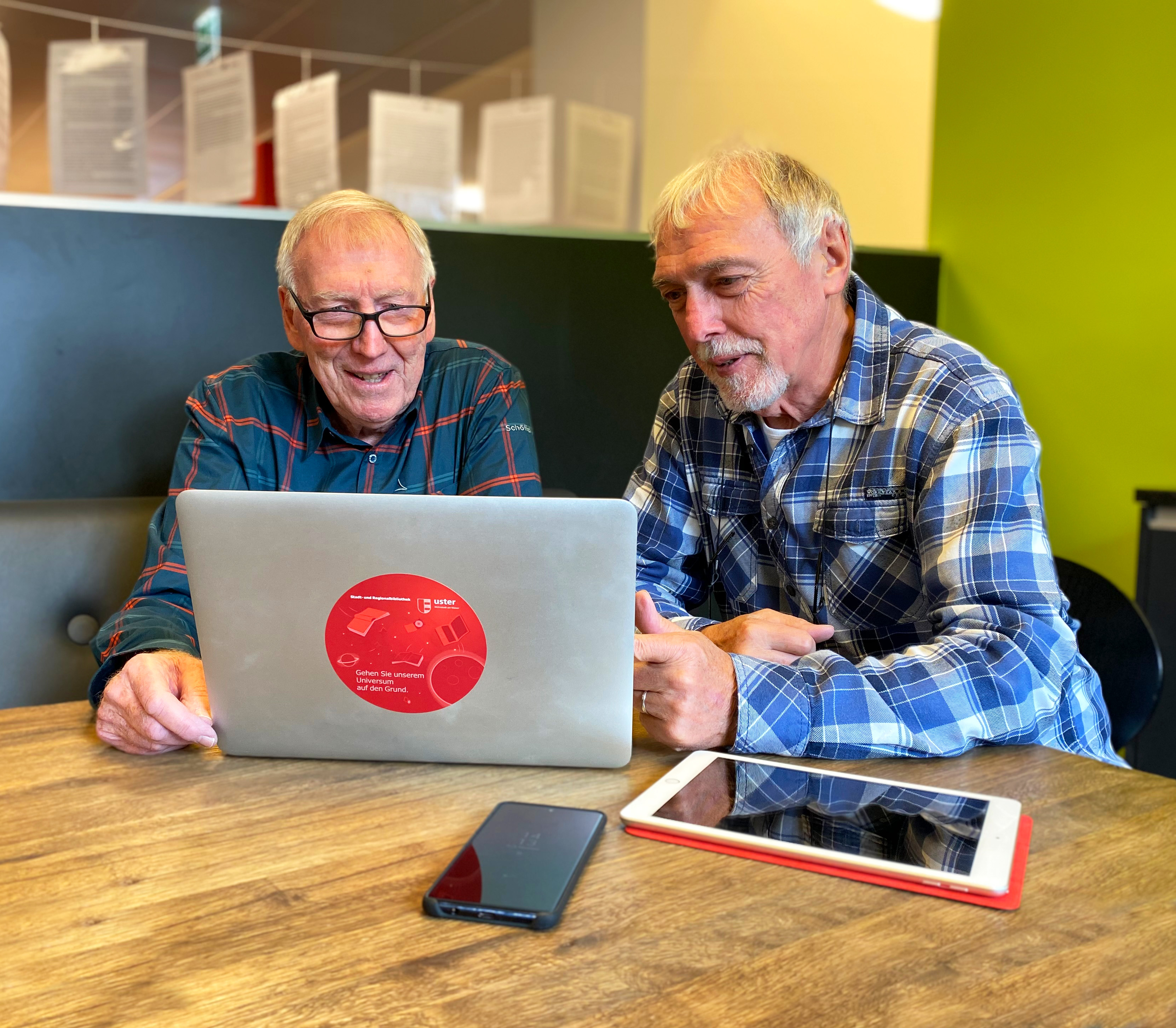Menschen höheren Alters sitzen an einem Tisch und schauen auf einen Computer. 