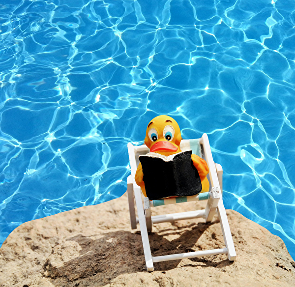 Gummiente im Liegestuhl vor Schwimmbadwasser
