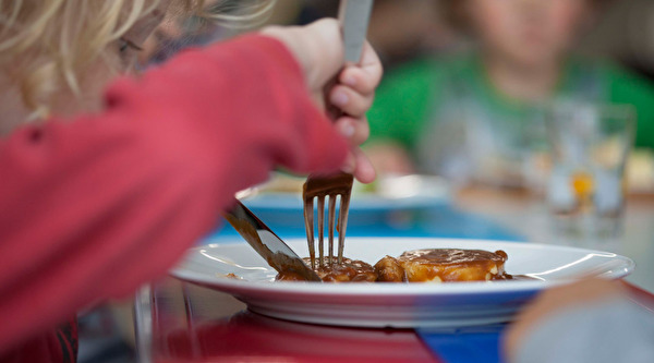 Kind schneidet im Teller sein Essen