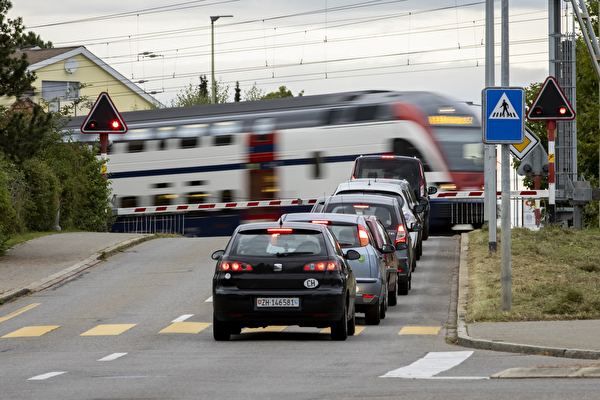 Autos warten an geschlossener Schranke vor durchfahrendem Zug