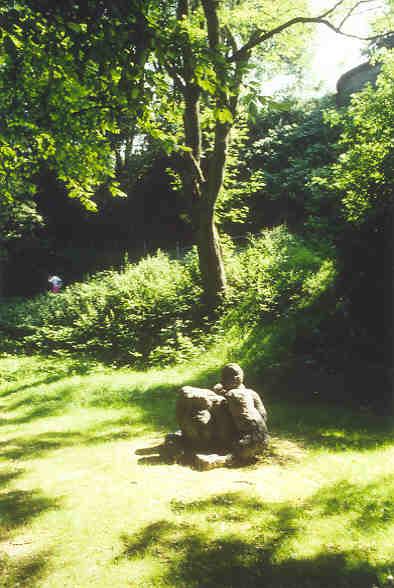 Rudolf Blättler, Luzern
(gestiftet durch die Gemeinde Wettingen)

In sich gekehrt sitzt sie da, den Rücken gegen die hohe Mauer, den Blick zur Limmat.  An einem schmalen Flecken Natur,  einer kleinen lauschigen Restidylle zwischen Verkehrshetze und dichtester Wohnform.  Der unscheinbare Ort  unter den Bäumen und zwischen den Sträuchern wird durch sie erst zum Platz. Ihre Urwüchsigkeit, ihre Kraft und Ruhe erfüllen den Ort, jedenfalls für jene, die sich selber die Musse nehmen, wie sie auf das Rauschen der Blätter und des Wassers zu hören, die hier den Lärm des Verkehrs und der menschlichen Siedlung vergessen machen.

Material: Bronze