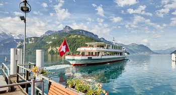 Ein Dampfschiff auf dem Vierwaldstättersee mit einer Schweizerfahne am Heck. 