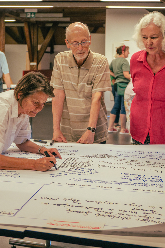 Menschen diskutieren und schreiben an einem Tisch auf Flipchart-Papier.