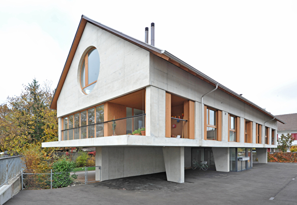 Haus auf Betonstelzen mit Sichtbetonfassade, markanten Fenstern, Parterrefläche frei