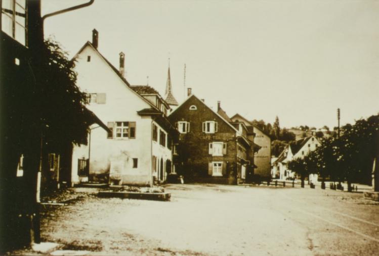 Blick auf die Metzgerei Ramstein (noch ohne modernen Ladenvorbau) in der Hauptstrasse.

Das dunkle Haus in der Mitte ist die Hypothekenbank im Erdgeschoss.

Datierung: vor 1951