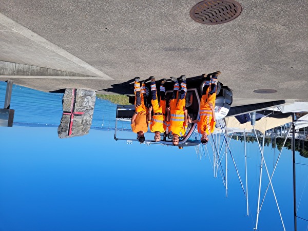 Vier in orange gekleidete Mitarbeiter stehen vor den Elektofahrzeug.