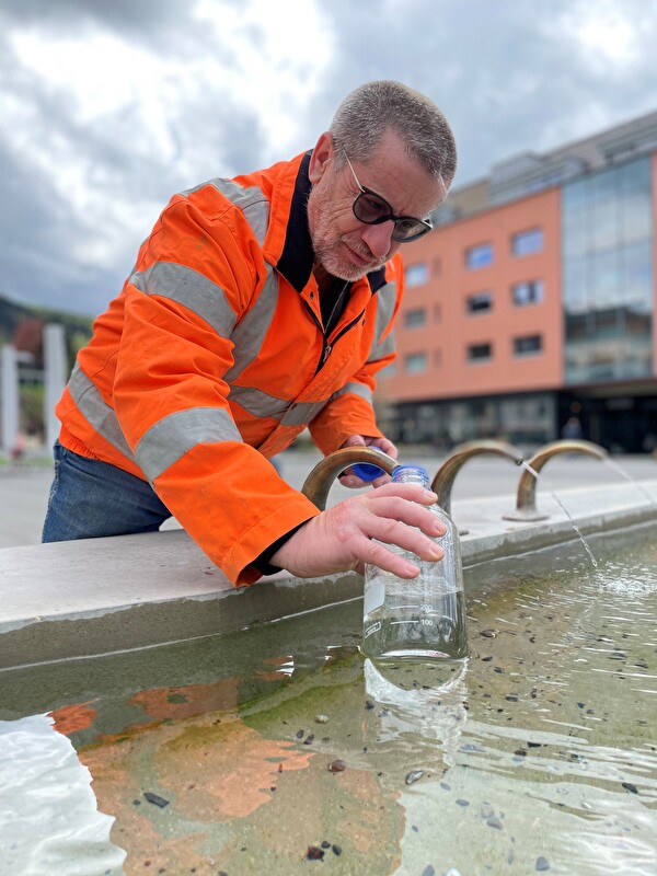 Brunnenmeister Peter Nussbaum befüllt eine Wasserflasche am Dorfplatzbrunnen.