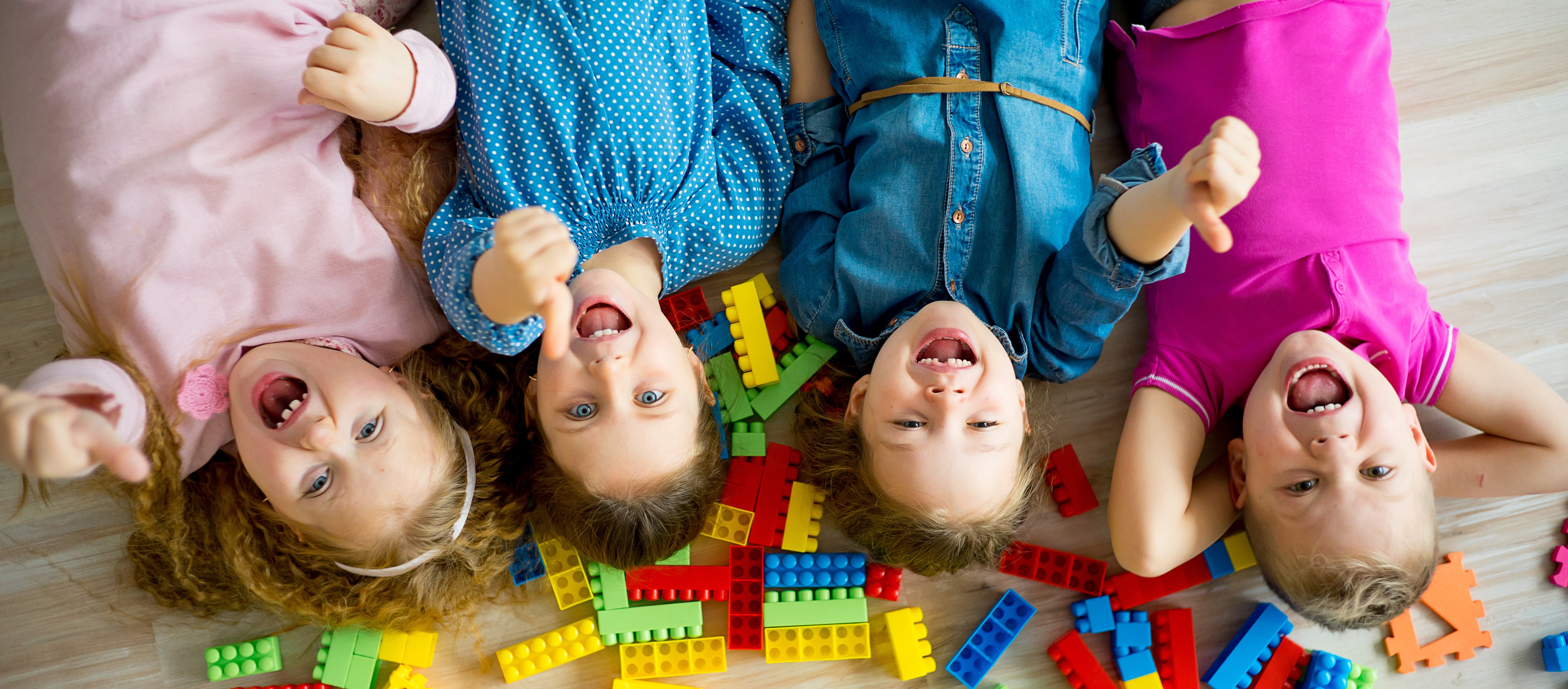 Bild von vier Kindern, die auf dem Rücken liegen, lachen und Daumen hoch halten