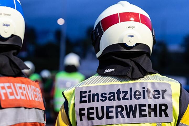 Bild von zwei Feuerwehrleuten von hinten mit Beschriftung Einsatzleiter Feuerwehr
