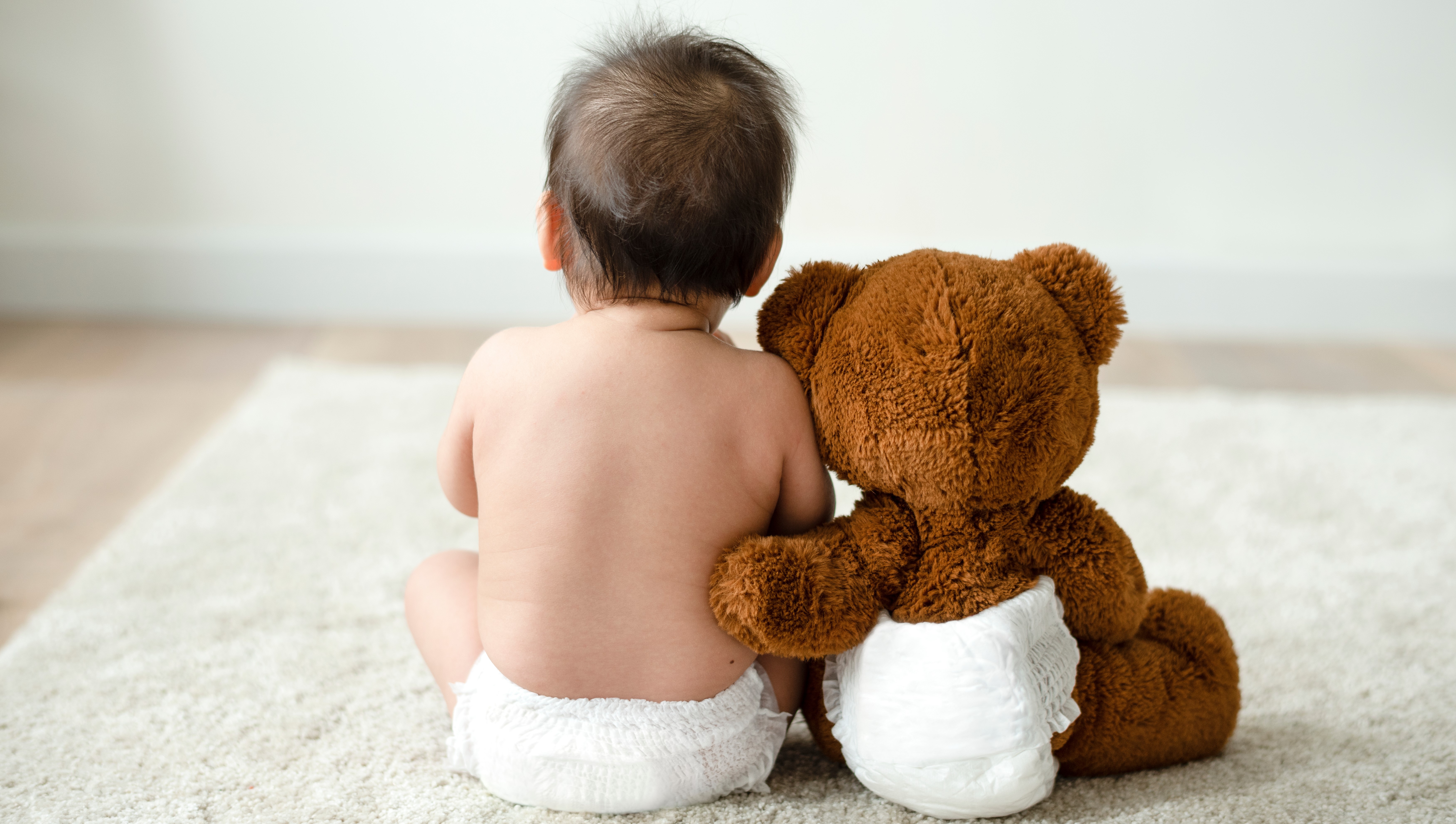 Bild von Kleinkind und Teddybär in Windeln von hinten