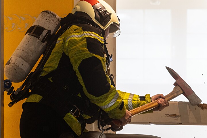 Bild eines Feuerwehrmannes mit einem Werkzeug der gerade eine Tür öffnet