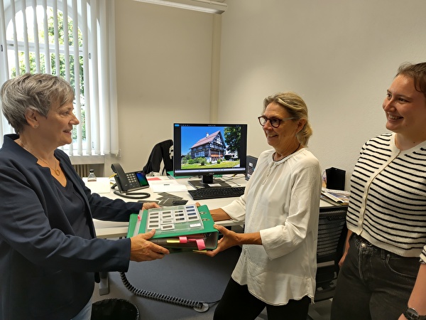 Legende: Maya Küng (links) übergibt symbolisch das Fotoarchiv ihres Mannes an die Archivarinnen der Gemeinde Gerda Leipold (Mitte) und Selina Sprecher (rechts).