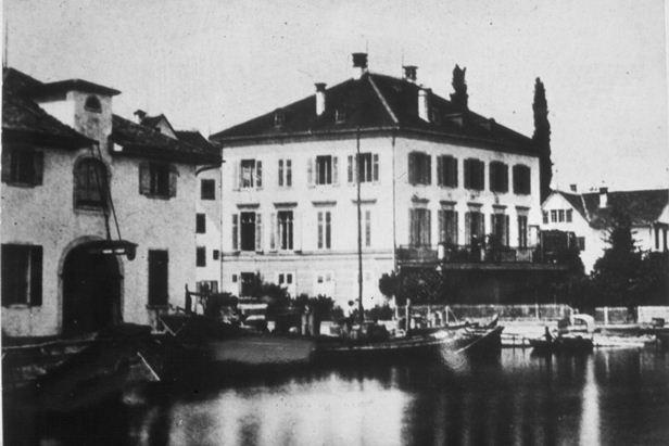 Das Bild zeigt den Hafen bei der Sust. Links Haus Sust, rechts Hotel Seehof, beide erbaut 1840. Der Hafen wurde 1874 beim Bau der Wädenswil-Einsiedeln-Bahn (heute Südostbahn) eingedeckt. Heute steht hier der Güterschuppen.