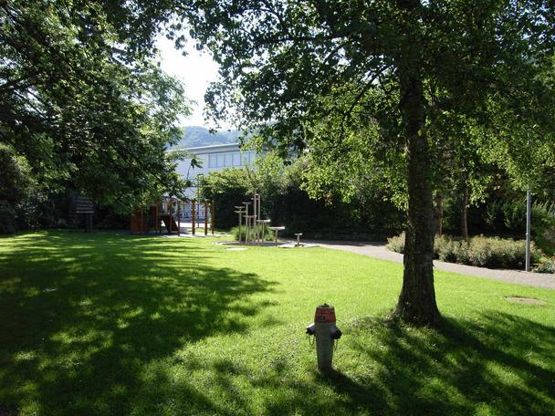 Idyllischer Park zwischen der katholischen Kirche und dem Schulhaus Wees, Au, mit einem gut unterhaltenen Spielplatz und Brunnen