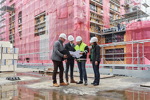 Eine Gruppe von Personen schaut auf einer Baustelle gemeinsam auf einen Plan.