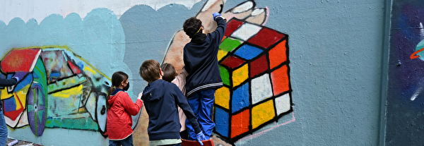 Kinder sprayen einen Rubikscube an eine öffentliche Wand.