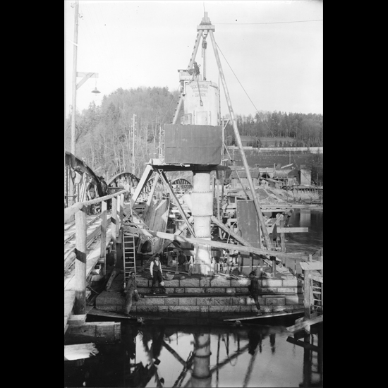 Die Verkleidung erfolgte vorzu mit fortschreitendem Aufbau und Absenken des Pfeilers. An der provisorischen Brücke ist ein Dienststeg angebracht, auf dem mit Kipploren Material transportiert wurde.