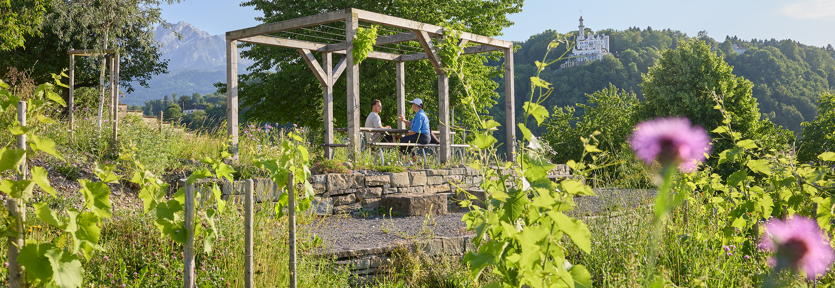 Zwei Passanten sitzen in der Pergola des Gartens geniessen die Naturoase