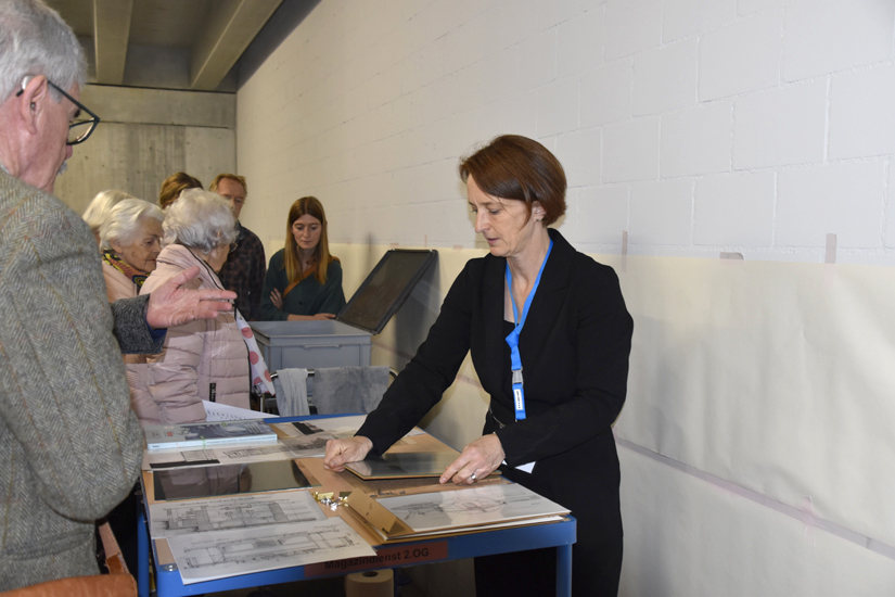 Während eines der Papiere erst ausgerahmt wird (vorne), verfolgt das Publikum bereits die Verwandlung des anderen grauen Papiers in einen leuchtend blauen Plan (hinten).