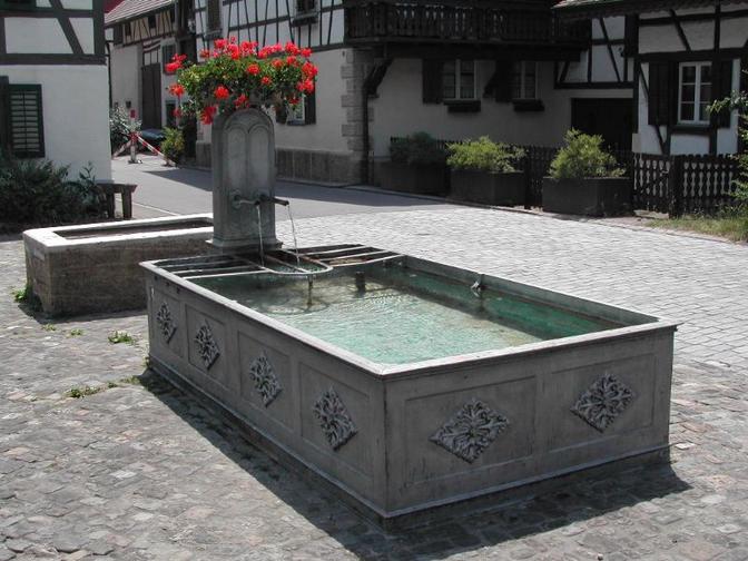 Wie sein Name besagt, ist der Brunnen eine Eisenkonstruktion aus dem Jahr 1850. Zwei Röhren speisen den Brunnen mit 18 Minutenliter aus einer eigenen Quelle. Der kleine Nebenbrunnen, völlig getrennt vom Hauptbrunnen, ist eine Steinkonstruktion und trägt keine Jahreszahl, dürfte aber sicher erst viel später erstellt worden sein.