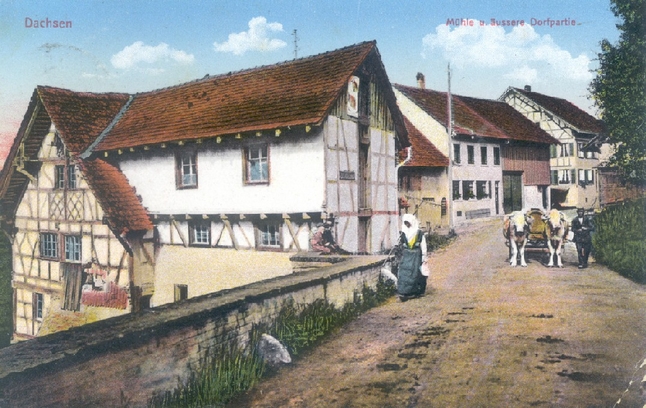 Es handelt sich um eine Ansichtskarte, die uns von Andre Moser zur Verfügung gestellt wurde. Sie trägt den Poststempel von 1924. Im Vergleich mit dem vorangehenden Holzfällerbild stellt man fest, dass in der Zwischenzeit bei der heutigen Liegenschaft Dorfstrasse 42 das Dach etwas angehoben worden ist.