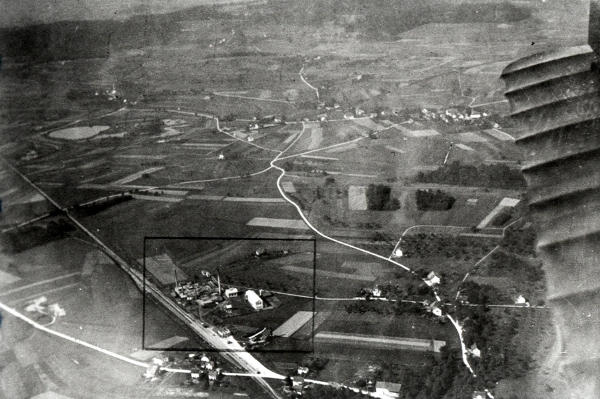 Aufnahme 1924
Dies dürfte die wohl älteste Luftaufnahme von Niederglatt sein. Sie wurde aus einem Militärflugzeug vom Typ DH-3 aus gemacht. Die Aufnahme zeigt die Elektroden-Fabrik Elektrocarbon und den Bahnhof Niederglatt (schwarzer Rahmen). Am unteren Bildrand ist das Restaurant Bahnhof zu erkennen. Im Hintergrund erkennt man Niederhasli und ganz links den Mettmenhaslisee. Rechts den stoffbespannten Flügel des Flugzeuges.