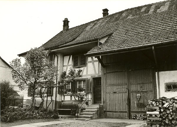 Foto 1965
Dieses Haus an der Bühlstrasse mit 2 Wohnungen, Scheune und Stall wurde 1764 gebaut. In der Stube des rechten Wohnteils wurde bis 1853 Sonntagsschule und Nähschule gehalten. Die Mädchen hatten in die Nähschule einen Schemel und im Winter zusätzlich ein Holzscheit zum Heizen mitzubringen. Der Hausteil links wurde 1958 umgebaut.