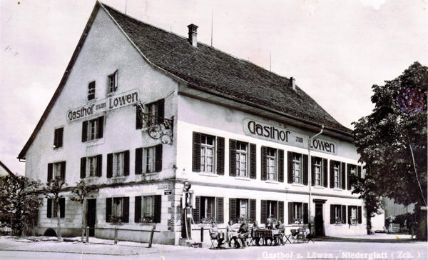 Foto 1940
Damals präsentierte sich der "Gasthof zum Löwen" noch als prächtiger Landgasthof, auf den man stolz sein konnte. Viele schmucke Details sind gegen Ende der 40er Jahre wegrenoviert worden. Das kunstvolle Wirtshausschild ist seit damals unauffindbar.Die markanten Ecksteine und das durchgehende Gesimse über dem Erdgeschoss belebten die Fassade und unter dem verkleideten Dachvorsprung entdeckt der aufmerksame Betrachter sogar noch Malereien.
Noch ist die Fassade so aussagekräftig, dass sogar die Zapfsäule an der Gebäudeecke nicht ungebührlich in Erscheinung tritt. (Text: Lo 1982)