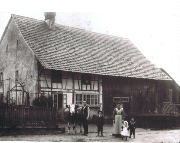 Foto: 11. Dezember 1904
Familie Julius Schmid vor ihrem Bauernhaus an der Grafschaftsstrasse (wo die heutige Post steht). Während den Jahren 1835-1841 schliefen in diesem Haus die Sekundarschüler aus Regensberg und Rümlang, weil der weite Schulweg eine tägliche Rückkehr nach Hause nicht zuliess. 