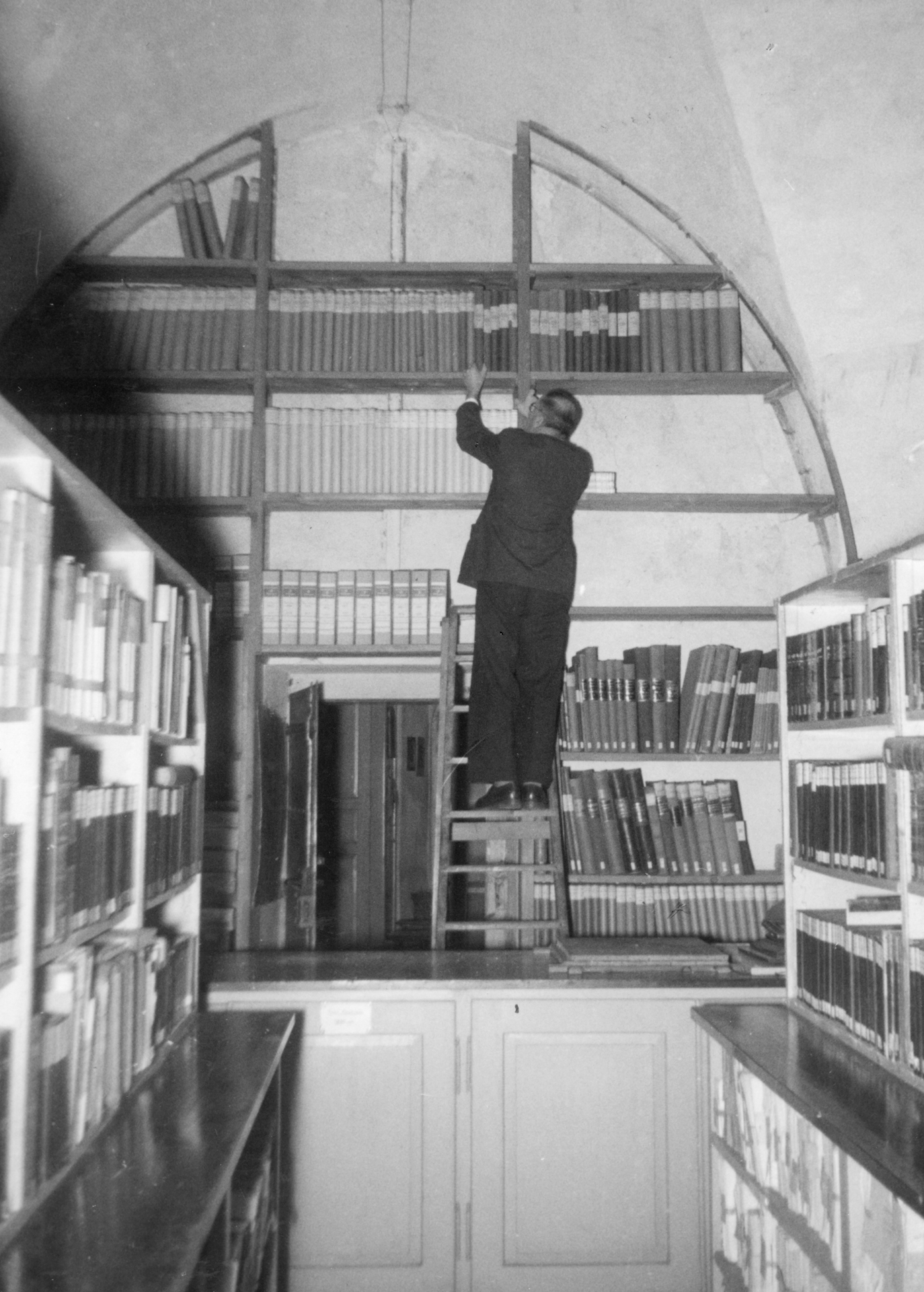 Fotografie des Kanzleisekretärs
Gaudenz Lütscher am Büchergestell
im Gewölbebogen des Stadtarchivs
Chur im Rathaus. (StadtAC, F 01.0215.001,
Foto Caspar, ca. 1928–1935).