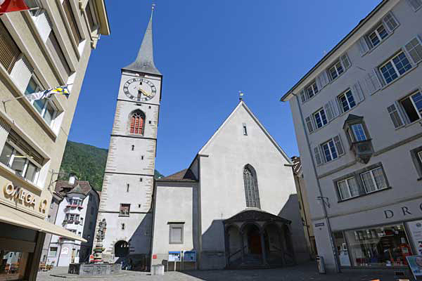 Der schmale Turm mit spitzem Helm und den grossen Zifferblättern. Rechts: Glasfenster von Augusto Giacometti.