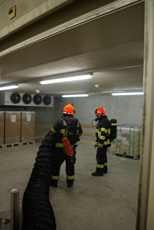 Die Feuerwehr beim Absaugen des Rauches in einem gefangenen Raum mittels Auer-Lüfter und unter Atemschutz.