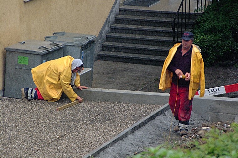 Bauarbeiter der Valli AG arbeiten bei strömendem Regen am Personalparkplatz.