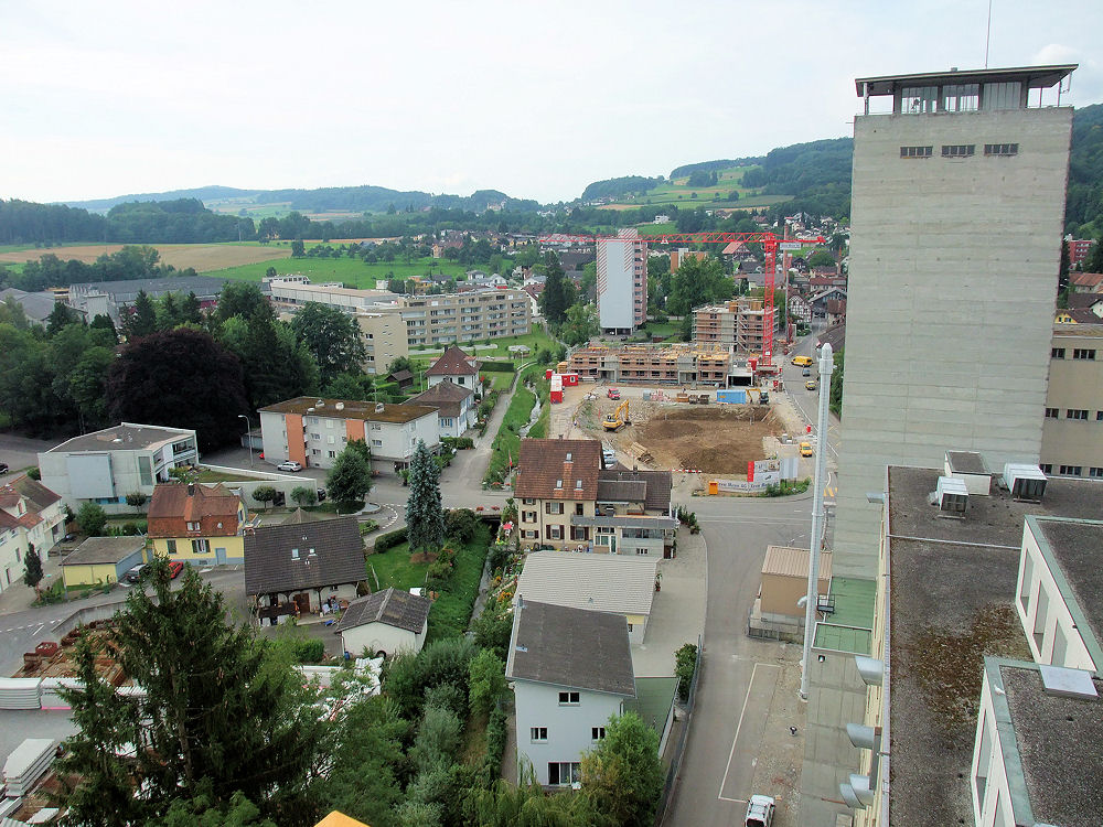 Auf dem Areal des ehemaligen Bahnhofs der Wohlen-Meisterschwanden-Bahn entsteht gerade eine Arealüberbauung mit 45 Wohnungen, Gewerbräumen und zwei Tiefgaragen. Neben der Baustelle der renaturierte Hinterbach. Hinter der Baustelle das schon sehr lange zum Ortsbild gehörende Hochhaus Wohlerstrasse 7. Links die neuen Wohnblocks Wohlerstrasse/Tannwinkel. Im Hintergrund: Der Sandbühl des Ortsteils Hilfikon.