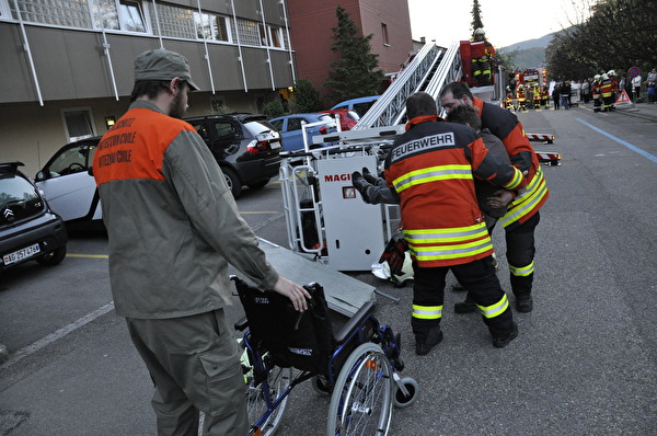 Die Gerettete Ursula Zysset wird von den Feuerwehrmännern von der Autodrehleiter gehievt  Im Vordergrund wartet der Zivilschützer mit einem Rollstuhl. 