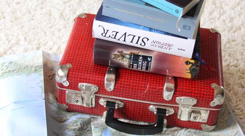 Ein Koffer im Sand, darauf einige Bücher aufgestapelt