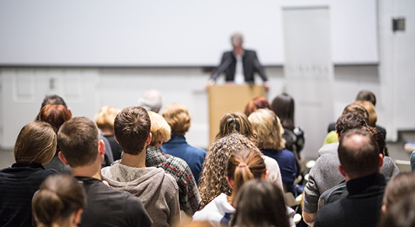 Photo d'une assemblée assise et d'un orateur