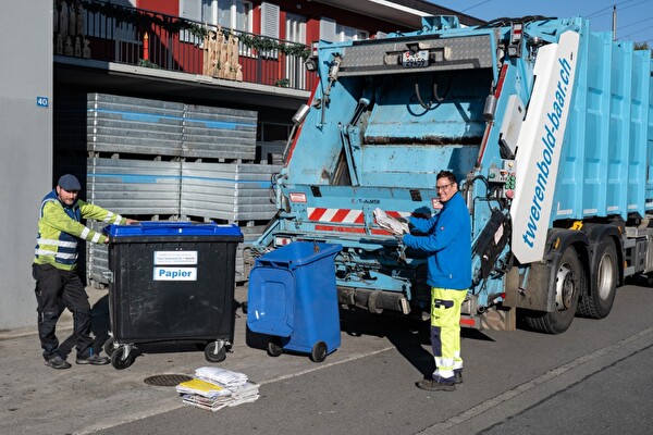 Entsorgungsfahrzeug der Franz Twerenbold AG mit zwei Mitarbeitern, die Papier in den Wagen laden.