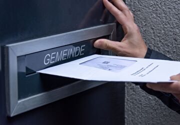 Eine Person wirft ein Stimmcouvert in den Gemeinde-Briefkasten 