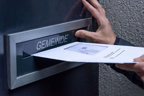Eine Person wirft ein Stimmcouvert in den Gemeinde-Briefkasten 