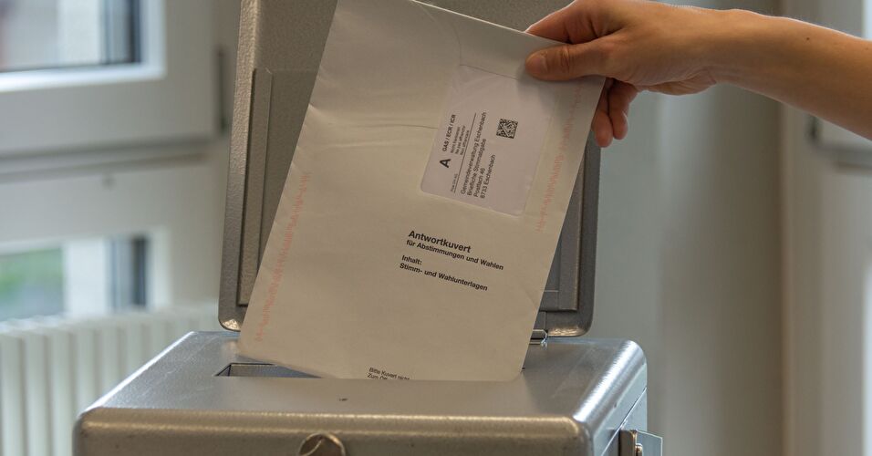 Stimmcouvert wird in die Urne eingeworfen