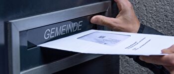 Eine Person wirft ein Stimmcouvert in den Gemeinde-Briefkasten 