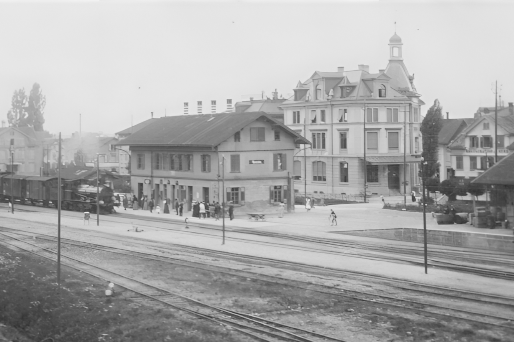 Der erste Bahnhof von 1856 und dahinter Post-/Gemeindehaus (heute Marktstübli) beim heutigen Marktplatz. Mit zunehmendem Bahnverkehr war die Schranke an Herisauerstrasse tagsüber teils bis 40 Minuten pro Stunde geschlossen. Deshalb wurde der Bahnhof 1913 nach Süden verlegt, ausserhalb der Siedlung. An den ersten Bahnhof erinnert noch heute das Hotel «alter Bahnhof» an der Herisauerstrasse.