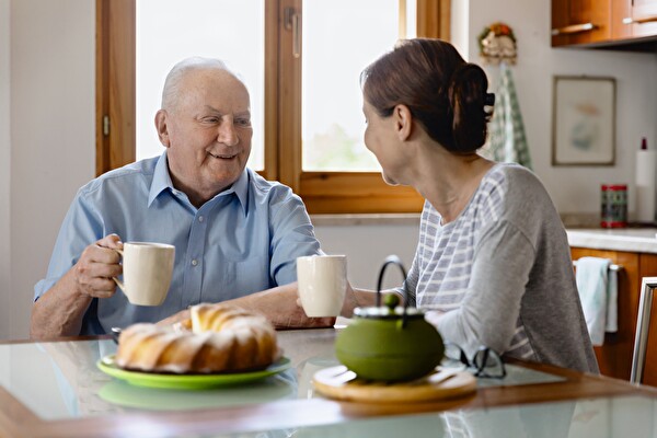 Links ein betagter Mann, rechts eine Frau. Beide befinden sich in einem Gespräch bei einer Tasse Tee.