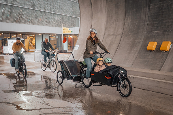 Zwei Männer auf einem Velo und eine Frau mit zwei Kindern auf einem Lastenrad.