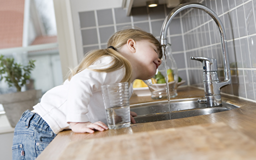 Ein Kind trinkt aus dem Wasserhahn.