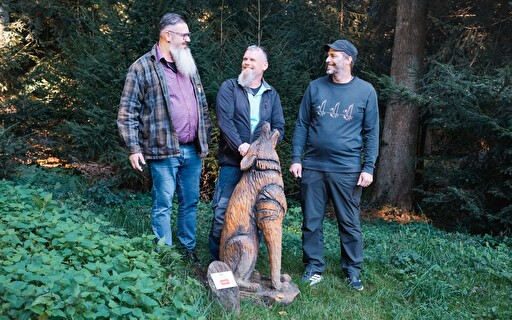 Drei Männer mit einer Holzfigur im Wald.