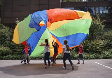 Kinder mit einem grossen, farbigen Tuch in der Luft.